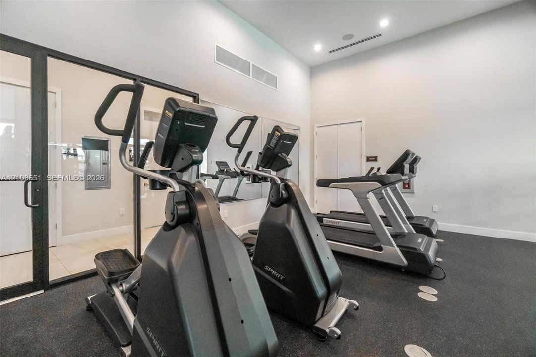 Fitness room featuring high ceilings, recessed lighting, full-wall mirrors, and black rubberized flooring enclosed by floor-to-ceiling glass paneling