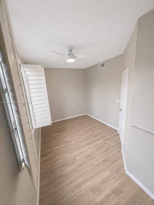Room featuring light-tone wood-finish flooring, white plantation shutters, a vaulted ceiling, and a modern ceiling fan with integrated lighting