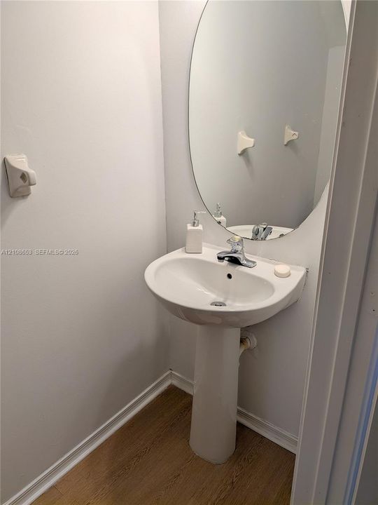 White ceramic pedestal sink featuring a polished chrome faucet, paired with an oval wall-mounted mirror and wood-finish flooring
