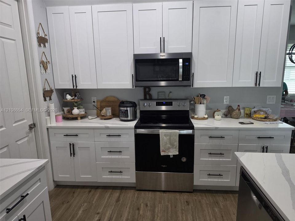 Kitchen featuring white shaker-style cabinetry, quartz countertops, stainless steel appliances, and wood-finish flooring