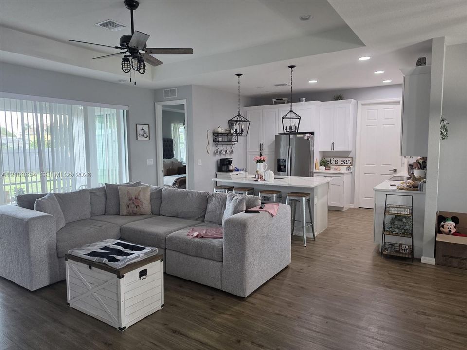 Open-concept kitchen featuring white shaker-style cabinetry, quartz countertops, a central island, and wood-finish flooring throughout