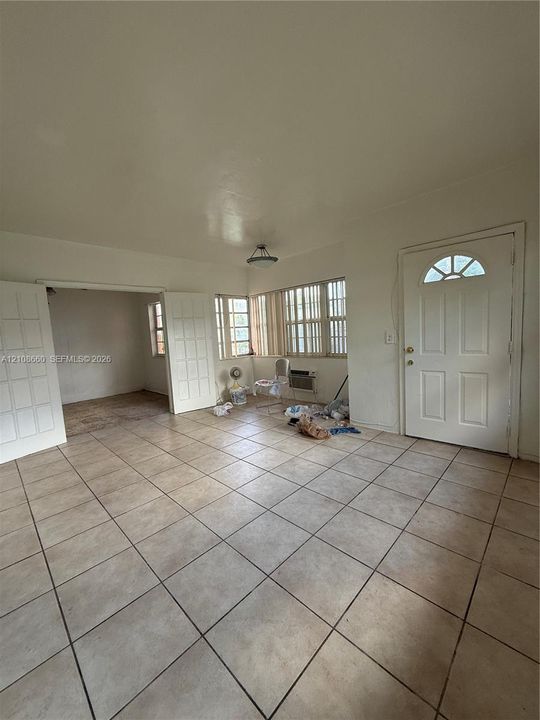 Interior space featuring neutral tile flooring, multiple sets of glass-paneled double doors, horizontal window blinds, and an exterior door with an arched glass insert