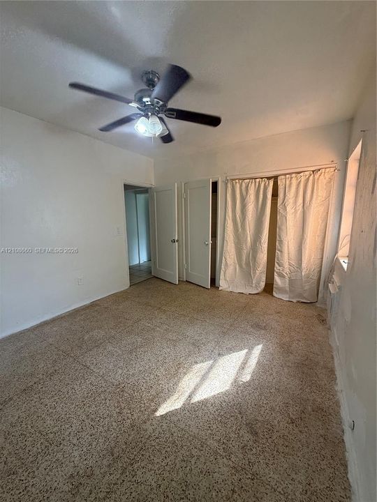 Interior space featuring speckled tile flooring, two solid-core doors, and a ceiling-mounted light fixture with a multi-blade fan