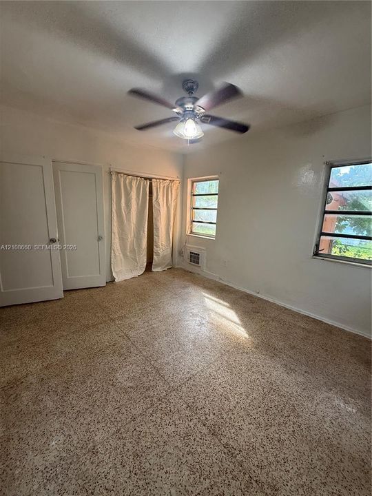 Interior space featuring terrazzo flooring, dual-panel doors, horizontal sliding windows, and a ceiling-mounted light fixture with a multi-blade fan