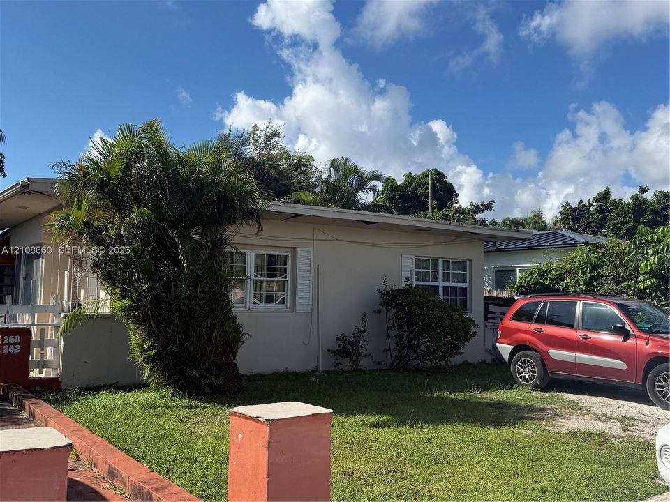 Single-story exterior featuring a flat roofline, stucco-finish siding, multi-pane windows with shutters, and a front yard with mature palm landscaping
