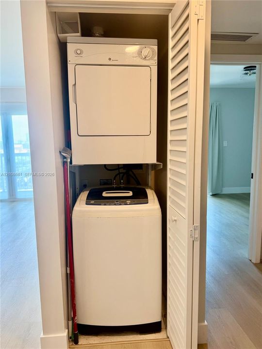 Laundry closet featuring a stacked washer and dryer unit enclosed by white louvered bi-fold doors