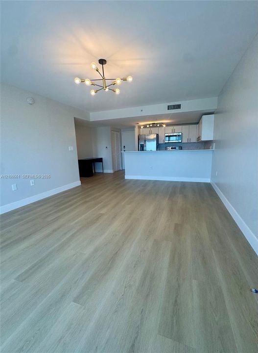 Open-concept space featuring wood-finish flooring, a multi-arm modern pendant light fixture, white cabinetry, stainless steel appliances, and a breakfast bar