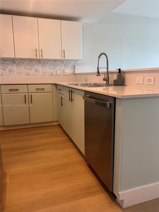 Kitchen featuring dual-tone cabinetry, wood-finish flooring, quartz countertops, a patterned tile backsplash, and stainless steel dishwasher