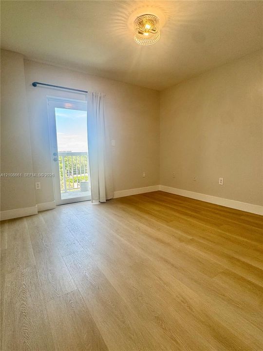 Interior space featuring wood-finish flooring, a flush-mount ceiling light fixture, and a glass-paneled door with access to an exterior balcony