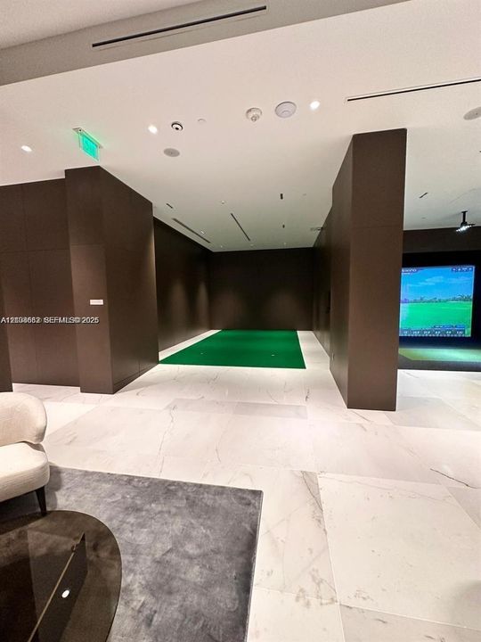 Indoor putting green featuring stone-tile flooring, dark wood-paneled walls, and integrated digital golf simulator