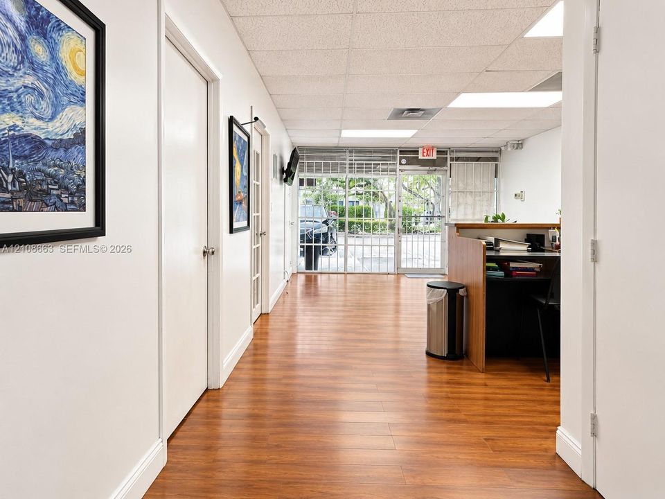 Wood-finish flooring, drop ceiling with recessed lighting, integrated wooden reception desk, and floor-to-ceiling glass panel entrance
