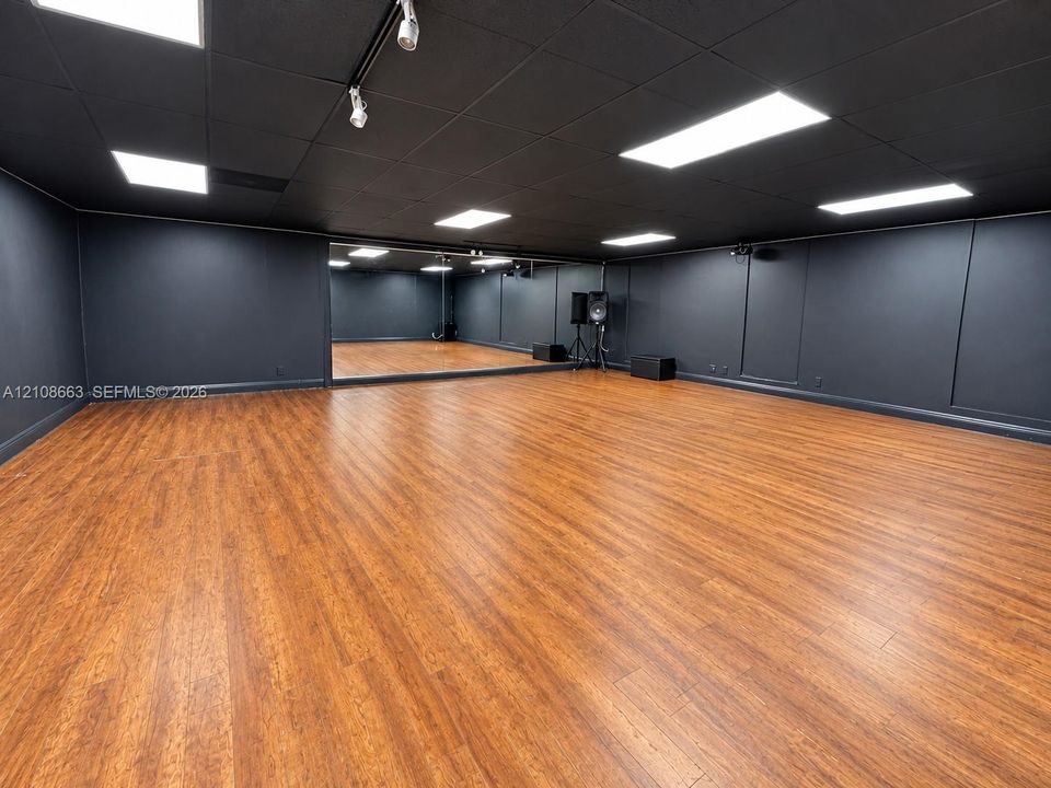 Dance Studio. Expansive multi-purpose room featuring wood-finish flooring, full-wall mirrors, recessed lighting, and a dark-toned drop ceiling