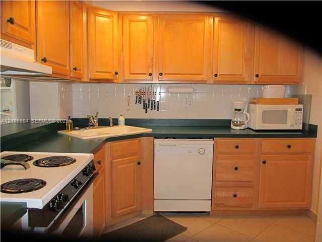 Kitchen featuring light wood cabinetry, white tile backsplash, solid-surface countertops, and tiled flooring