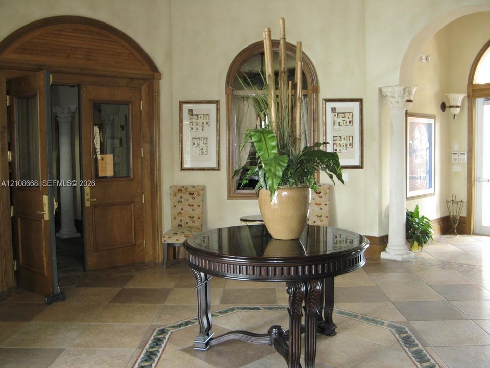 Foyer featuring arched wood double doors, decorative column, tile flooring with intricate border inlay, arched window, and wall-mounted sconce lighting