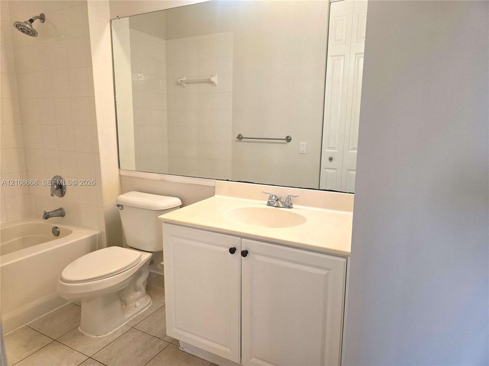 Bathroom featuring a white vanity cabinet, solid-surface countertop with an integrated sink, full-width wall mirror, and a tile-surround combination tub and shower