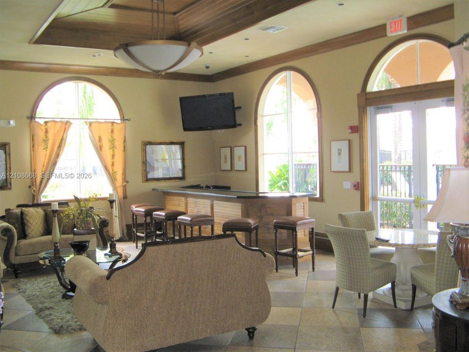 Tray ceiling with recessed lighting, arched windows, tile flooring, and a built-in bar with dark stone countertop