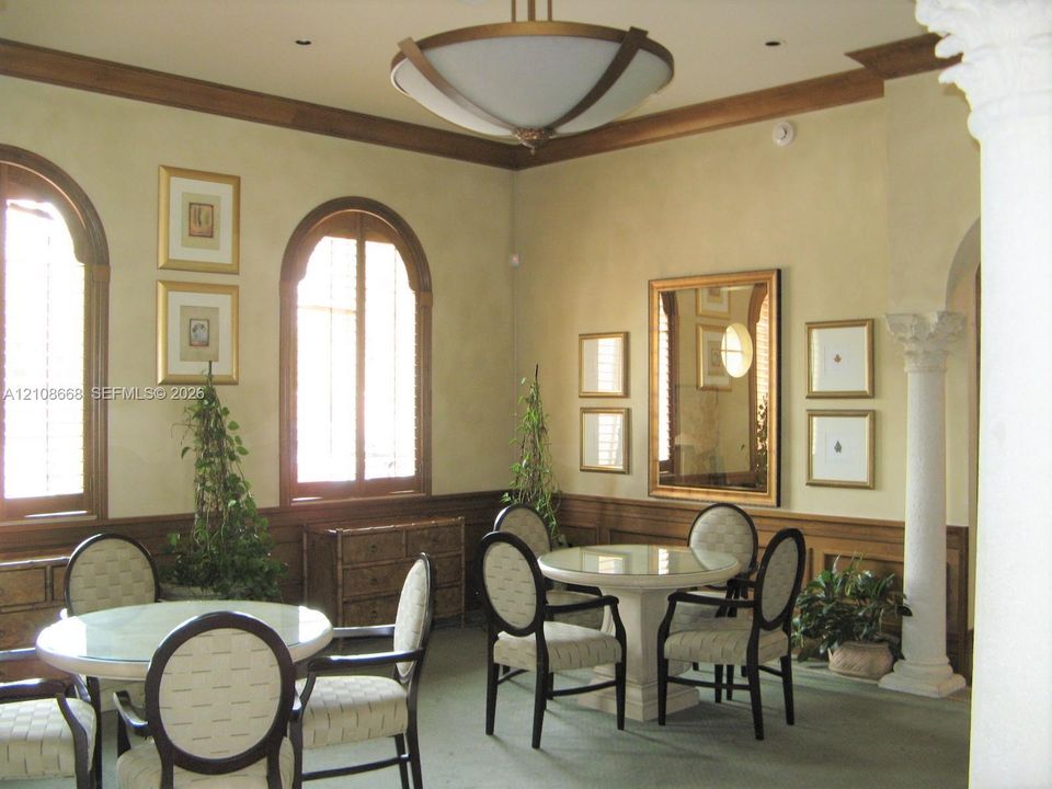 Interior space featuring arched windows with wood-trim detailing, decorative crown molding, a central modern chandelier, and a structural column with a Corinthian-style capital