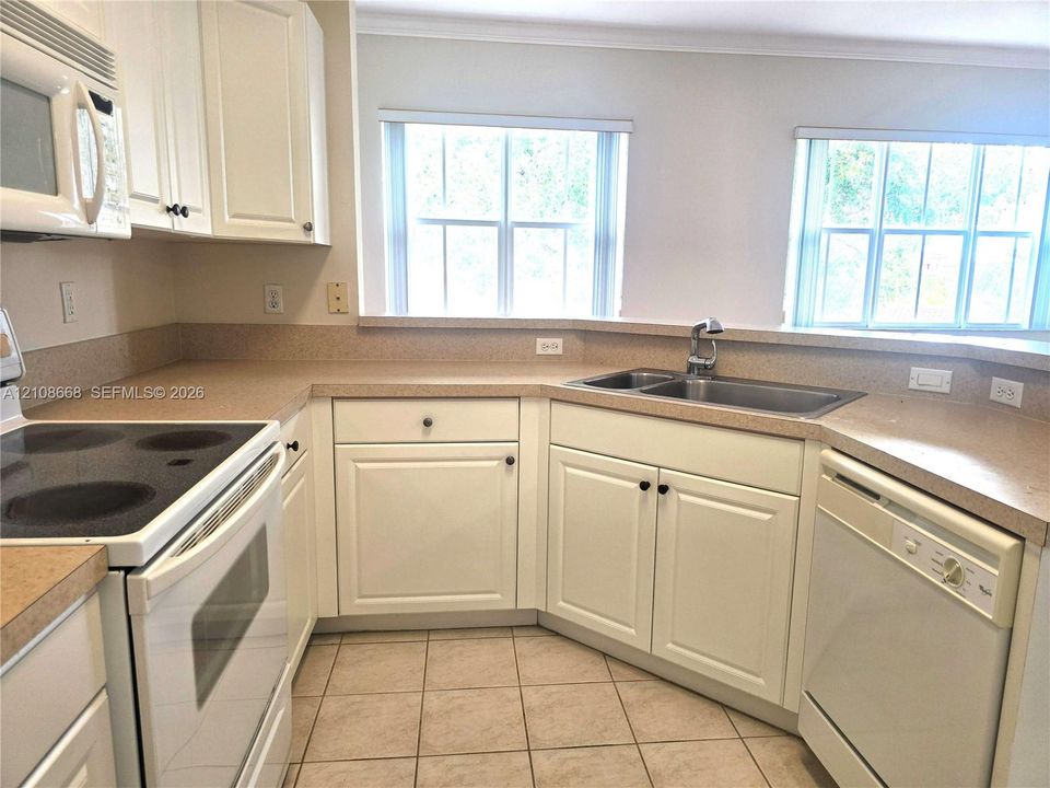 Kitchen featuring white shaker-style cabinetry, solid-surface countertops, a stainless steel double-basin sink, and ceramic tile flooring