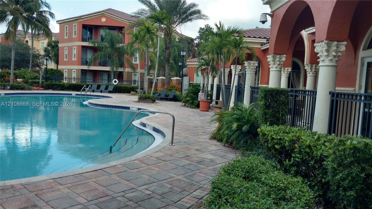 Swimming pool with integrated entry stairs, surrounded by a paver deck, ornamental columns, and mature landscaping
