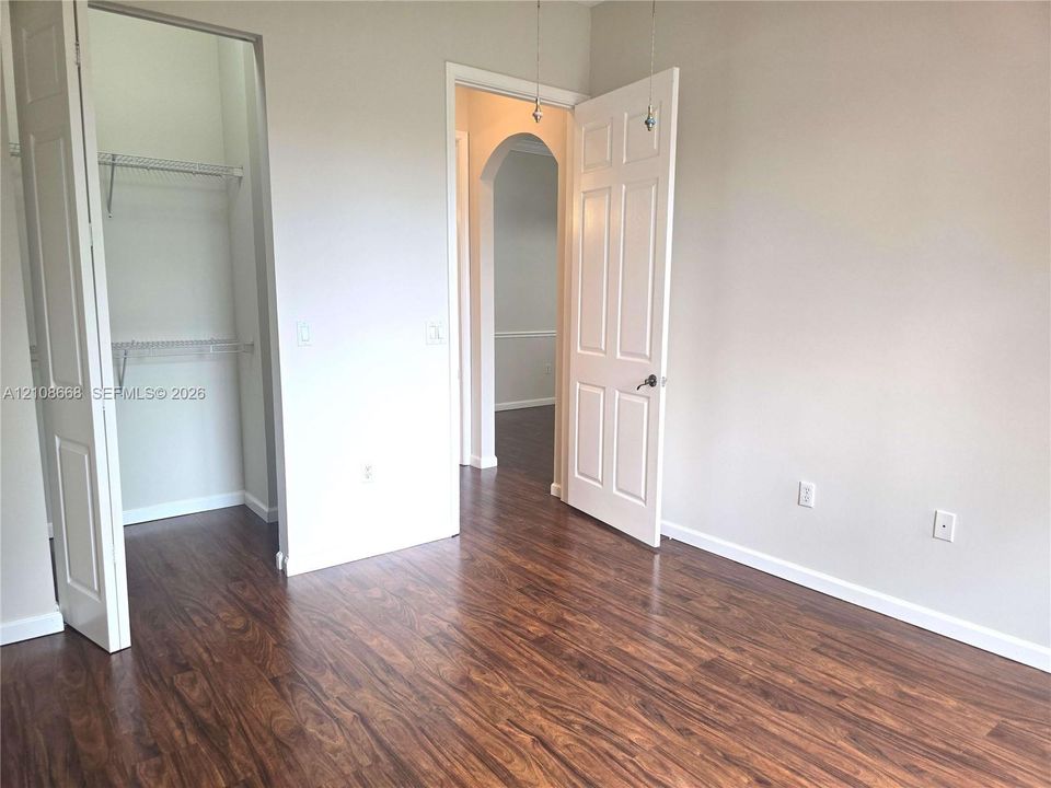 Room featuring wood-finish flooring, a multi-panel door, an arched entryway, and a built-in closet with wire shelving