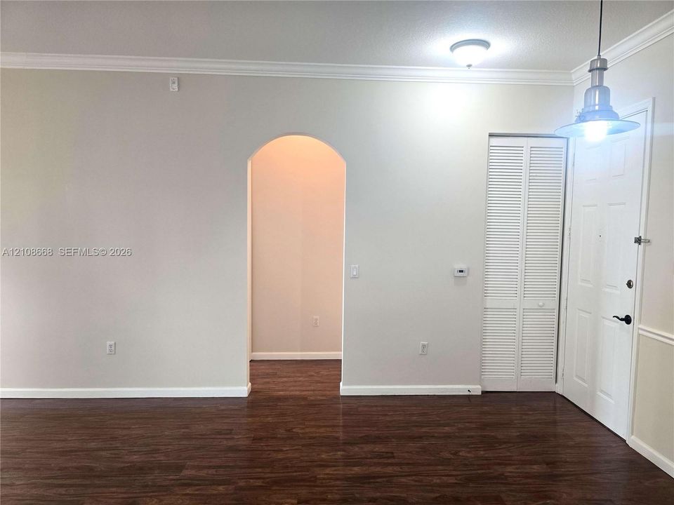 Interior space featuring wood-finish flooring, an arched architectural opening, crown molding, a louvered bi-fold closet door, and a metal pendant light fixture