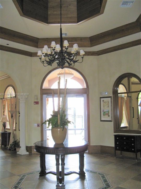 Foyer featuring a coffered octagonal ceiling with wood-finish trim, a prominent iron chandelier, arched doorways, tiled flooring with an inlaid decorative border, and a decorative column