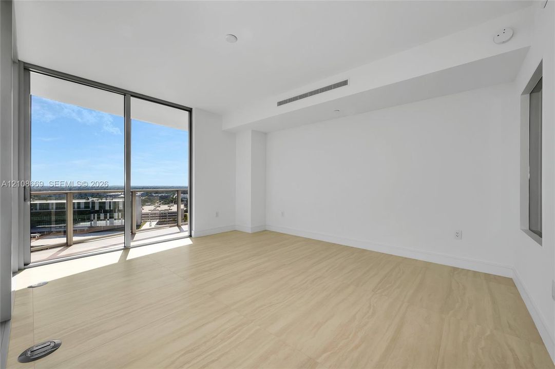 Floor-to-ceiling glass sliding doors, private balcony, wood-finish flooring, and minimalist white interior walls