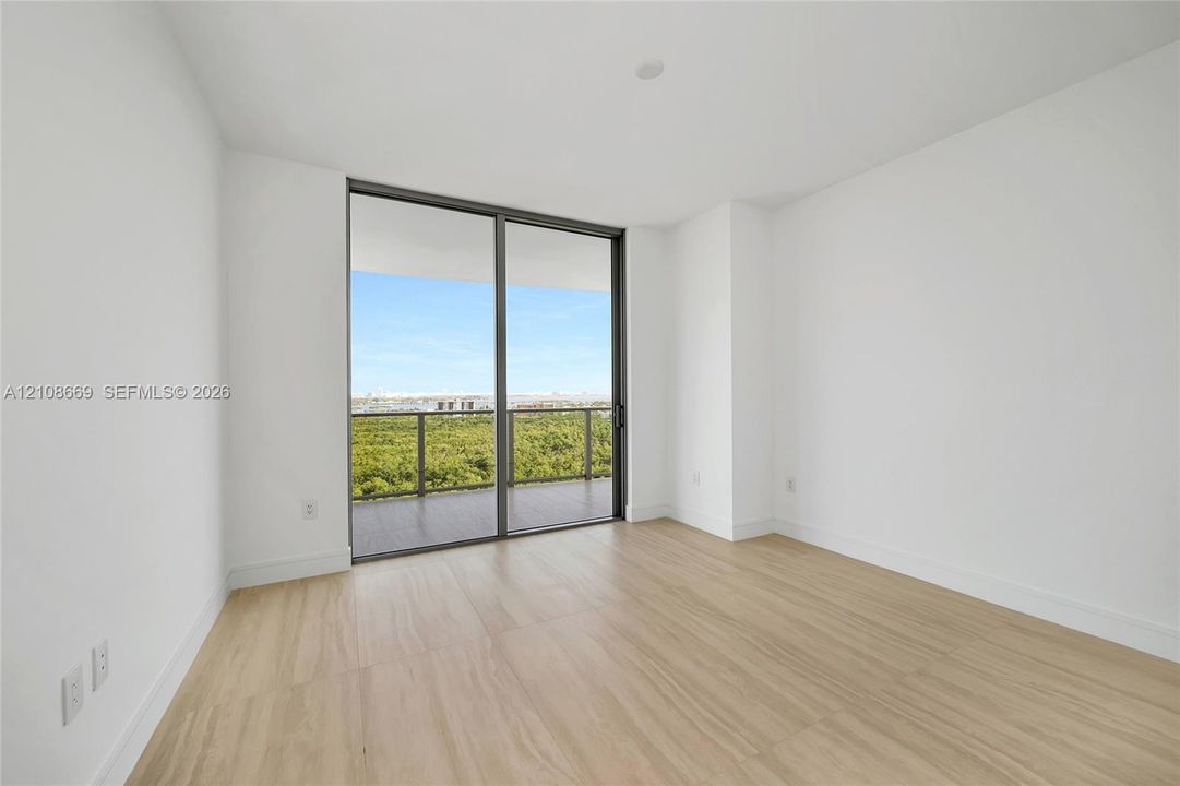 Floor-to-ceiling sliding glass door, private balcony with metal railing, and wood-finish flooring