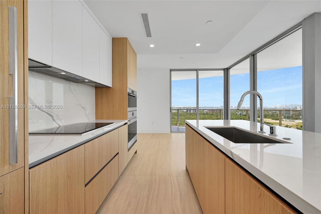 Modern kitchen featuring wood-finish cabinetry, white stone countertops, a full-height stone backsplash, stainless steel built-in double ovens, and floor-to-ceiling glass windows