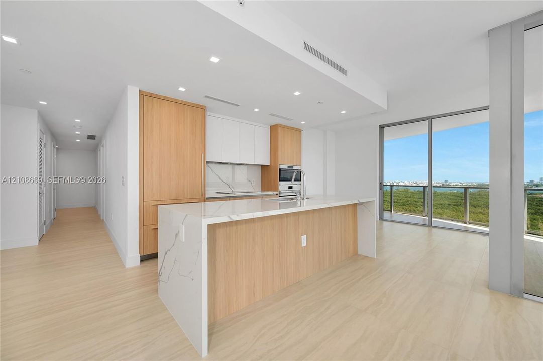 Kitchen featuring wood-finish cabinetry, stone-surfaced waterfall island, integrated appliances, recessed lighting, and floor-to-ceiling glass sliding doors