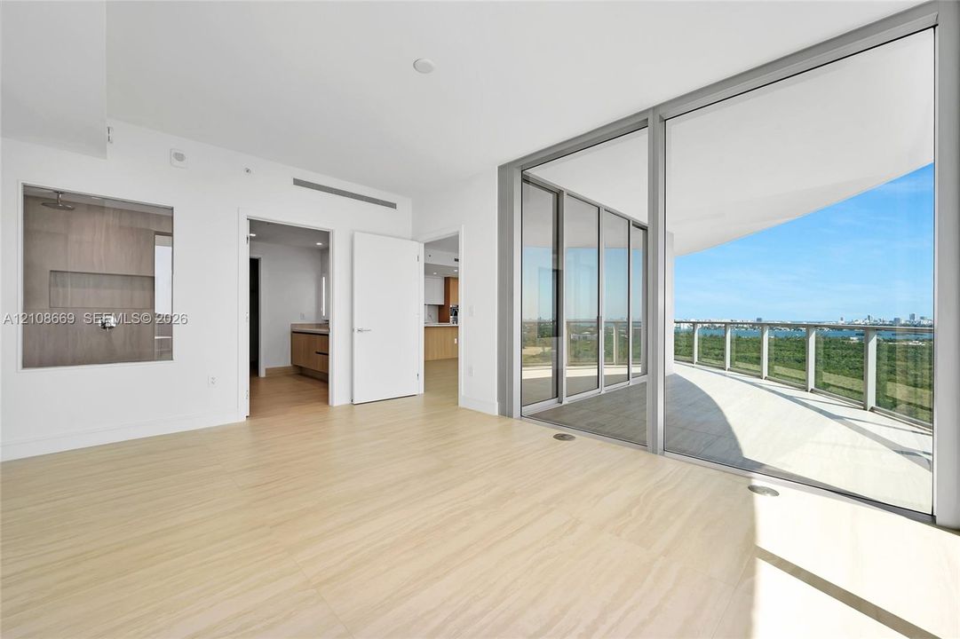 Interior space featuring wood-finish flooring, floor-to-ceiling sliding glass doors, a wrap-around balcony with a metal railing, and a glass-enclosed shower with tiled wall surrounds
