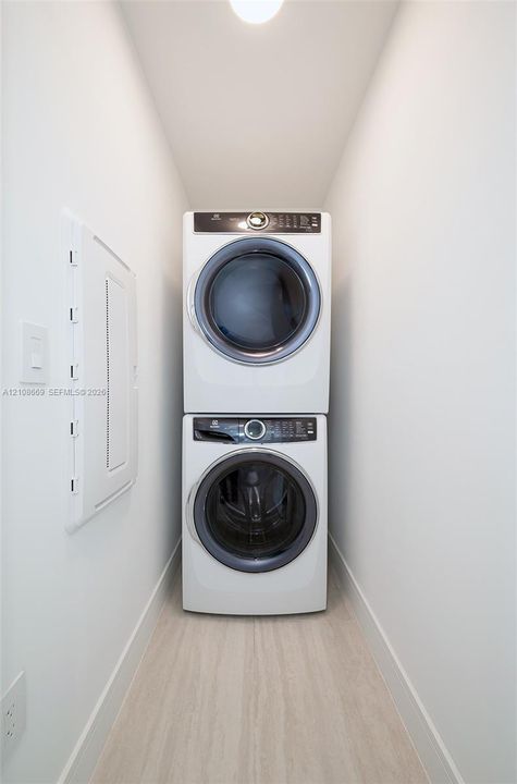 Dedicated laundry alcove featuring a stacked white front-loading washer and dryer set on light-toned wood-finish flooring