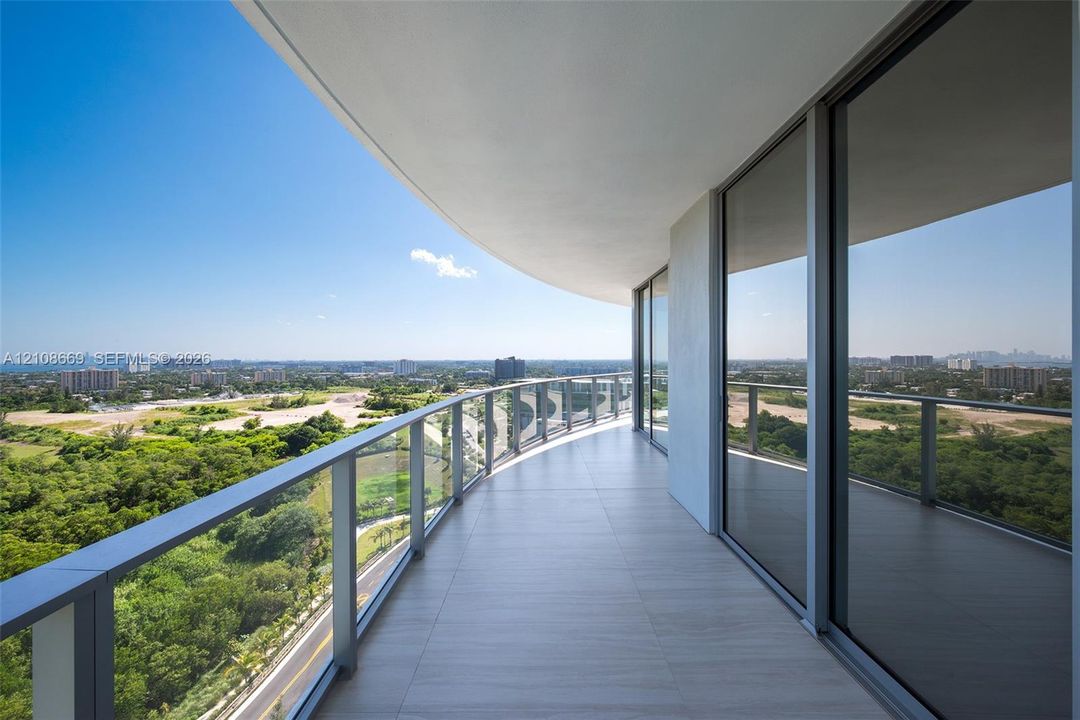 Curved balcony featuring large-format tile flooring, a glass and metal railing, and floor-to-ceiling sliding glass doors