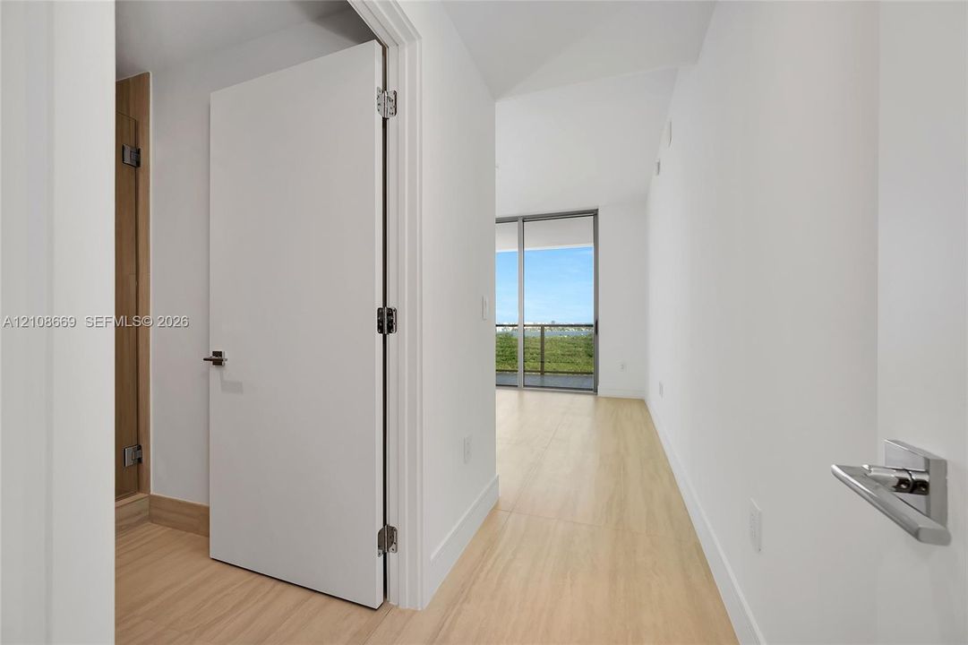 Interior space featuring wood-finish flooring, white walls, flush-panel doors, modern lever-style hardware, and floor-to-ceiling sliding glass doors