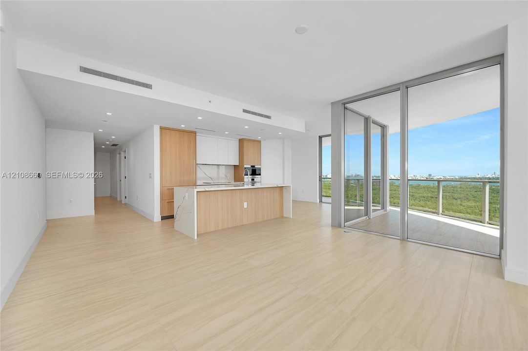 Open-concept interior featuring wood-finish flooring, kitchen island with stone-surface countertop, floor-to-ceiling glass sliding doors, and built-in stainless steel wall oven