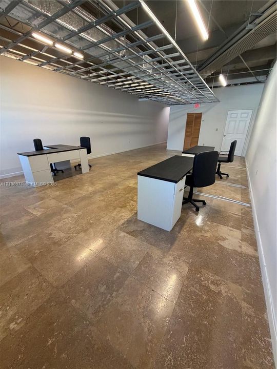 Open-concept commercial space featuring stone tile flooring, exposed industrial-style ceiling grid, and recessed linear lighting