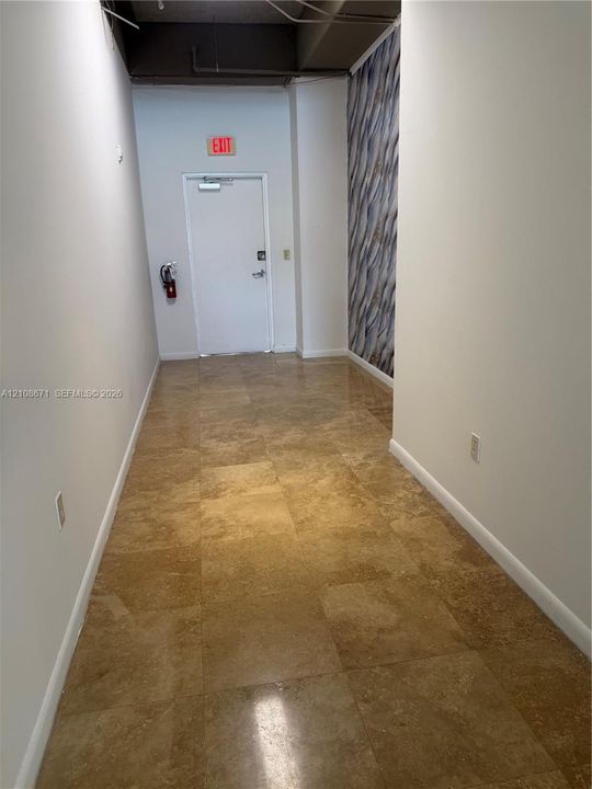 Hallway featuring polished stone-finish tile flooring, an accent wall with patterned wall covering, and an exposed industrial-style ceiling