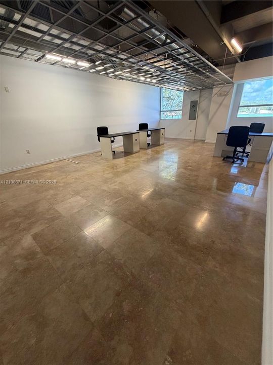 Open-concept interior featuring large-format stone tile flooring, exposed metal ceiling grid, and multi-paned windows