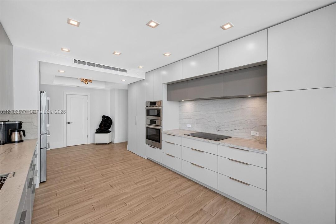 Modern kitchen featuring matte finish cabinets, stone counters & backsplash, built-in stainless steel double wall ovens, cooktop, and wood look plank porcelain flooring
