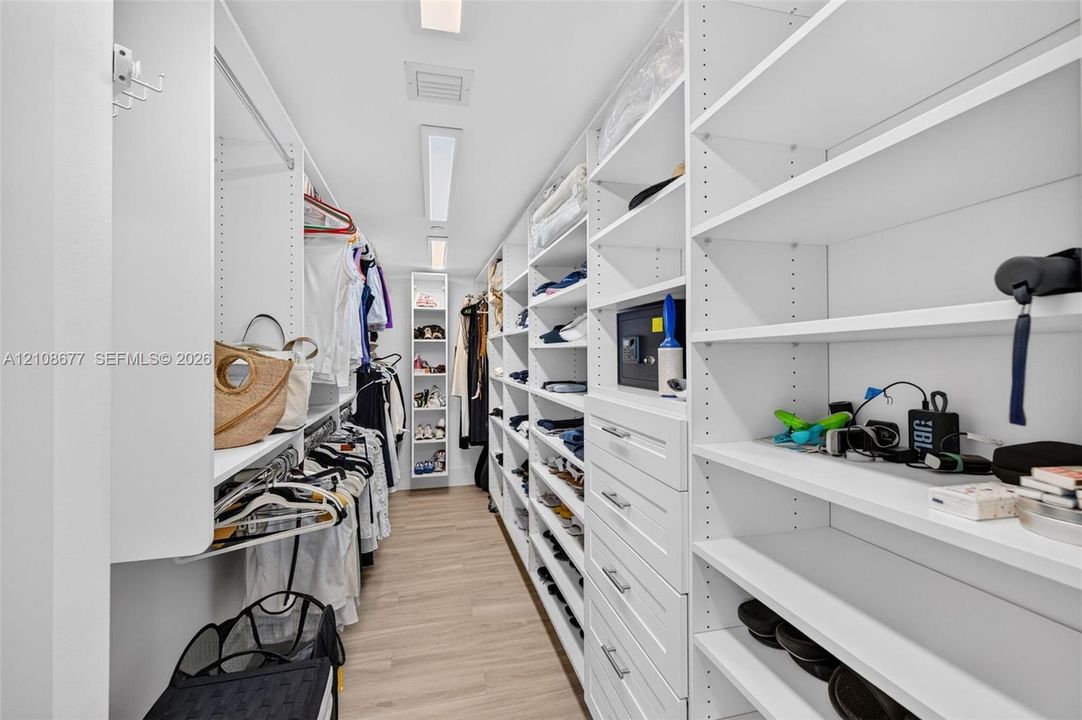 View toward long side of the custom walk-in closet featuring floor-to-ceiling white shelving, integrated cabinetry with drawers, multiple hanging rods, and wood look plank porcelain  flooring