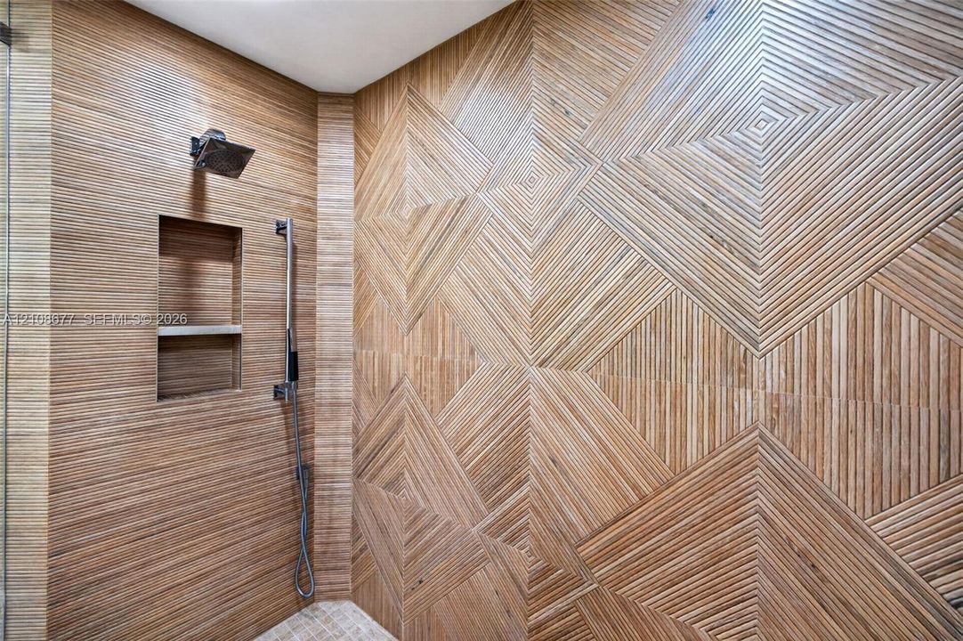 Shower enclosure featuring intricate geometric wood-look wall tile, recessed shampoo box niches, a, and a handheld spray fixture