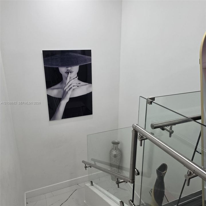 Staircase featuring a frameless glass railing with polished metal hardware and tile flooring