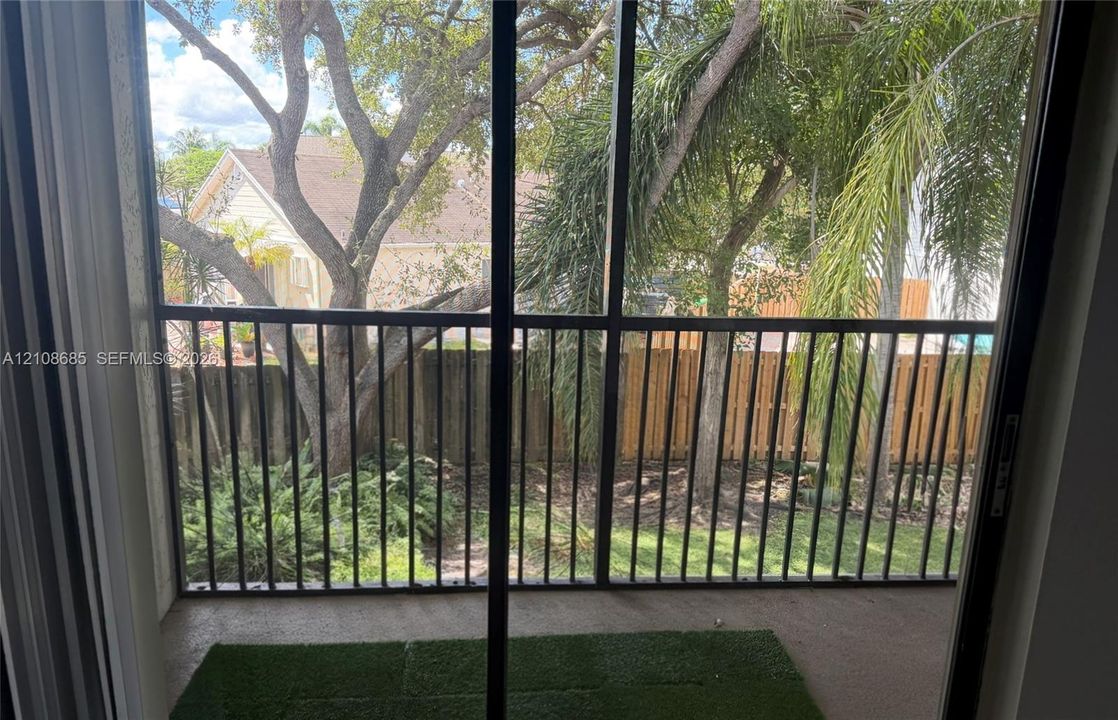 Screened-in balcony featuring black metal railings, concrete flooring, and synthetic turf inlay