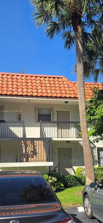 Multi-level exterior featuring a terracotta tile roof, stucco finish, and black metal balcony railings