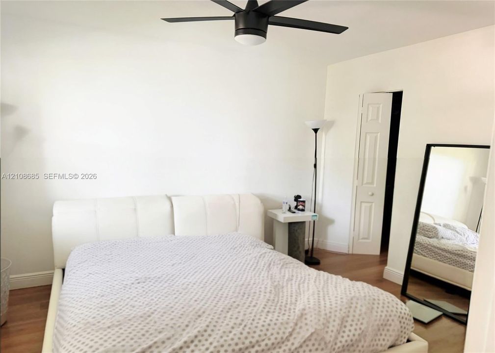 Room featuring wood-finish flooring, a matte black multi-blade ceiling fan with integrated lighting, and a six-panel interior door