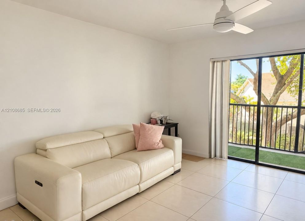 Neutral-tone tile flooring, white wall finishes, ceiling fan with integrated lighting, and sliding glass doors with direct access to a private balcony
