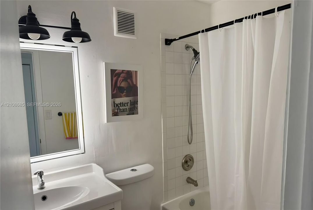 Bathroom featuring a vanity with an integrated sink, matte black dual-bulb wall-mounted lighting, and a bathtub with white tile surround and a handheld shower fixture