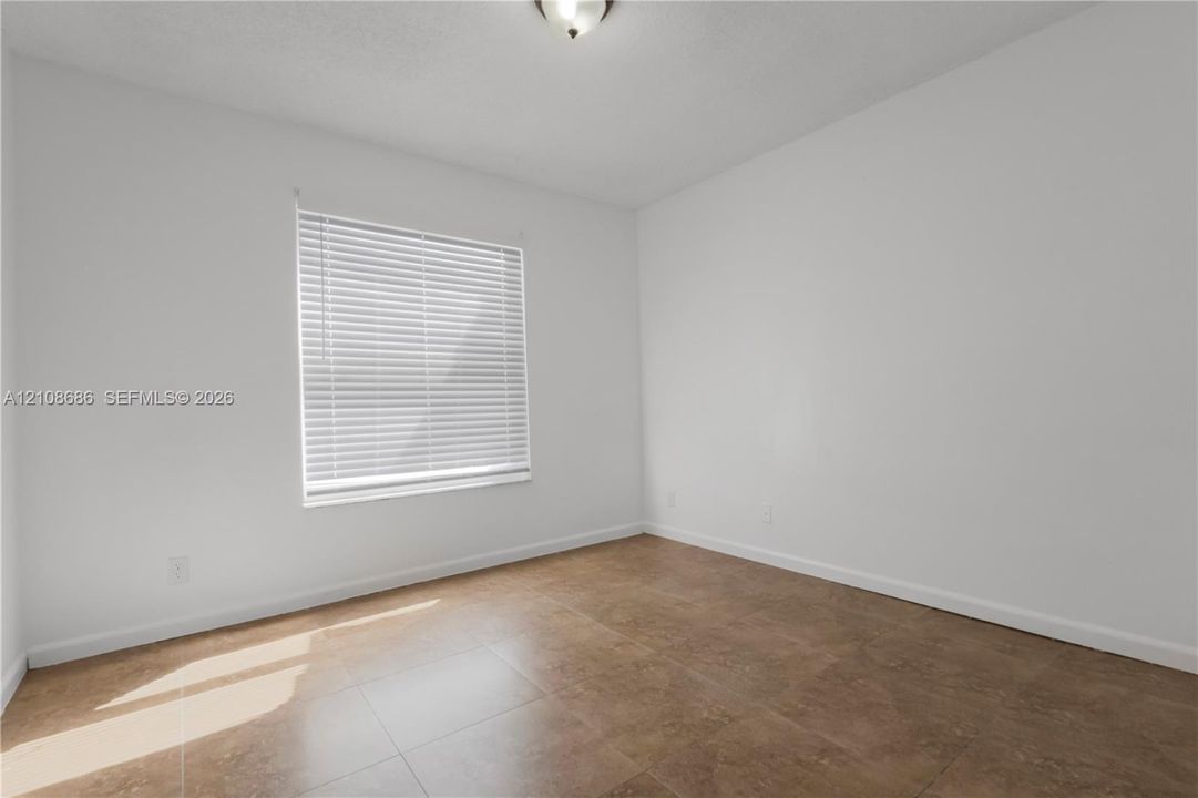 Interior room featuring large-format ceramic tile flooring, neutral wall tones, a single-window configuration with horizontal blinds, and a central ceiling-mounted light fixture
