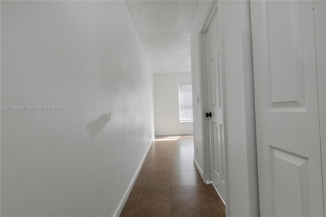 Hallway featuring large-format neutral floor tile, smooth-finish walls, and a multi-panel interior door with a matte black lever handle