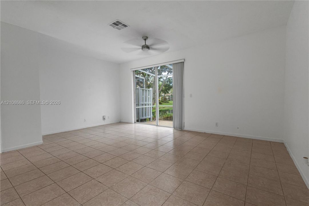 Interior space featuring neutral-toned tile flooring, a ceiling fan, and sliding glass doors that open to an outdoor screened enclosure
